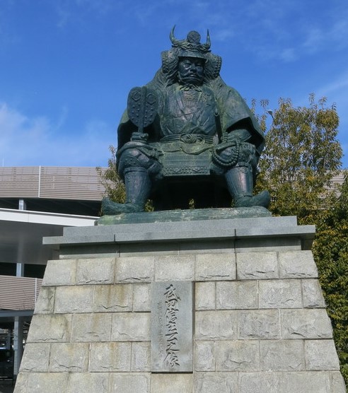 甲府駅前に、床几に腰掛け軍配を握った武田信玄公銅像が鎮座している